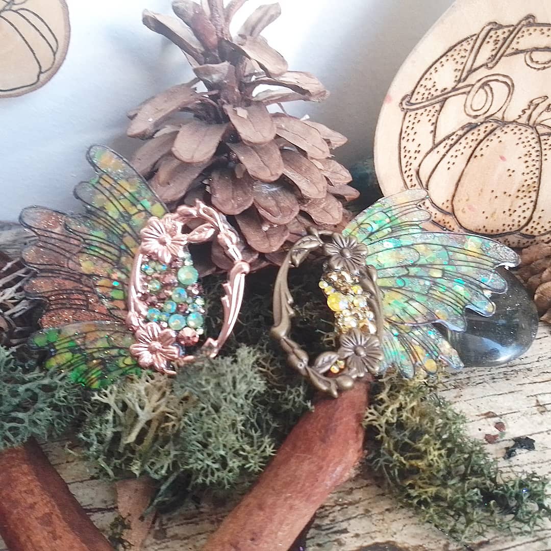 Broches ailes de libellule irisees roses et dorees posees sur des pommes de pin, decor automnal