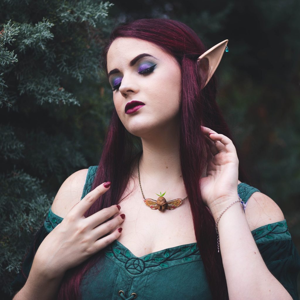 Portrait d'une femme aux oreilles elfiques portant un collier insecte dore, robe verte