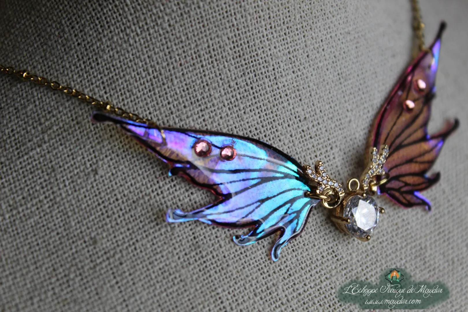 Collier aile de papillon bleue et rose avec couronne doree et cristal, vue rapprochee