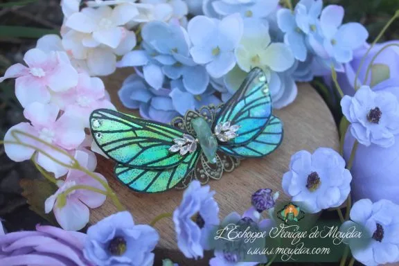 Barrette cheveux grandes ailes de papillon vert turquoise avec filigrane strass, sur fond de fleurs