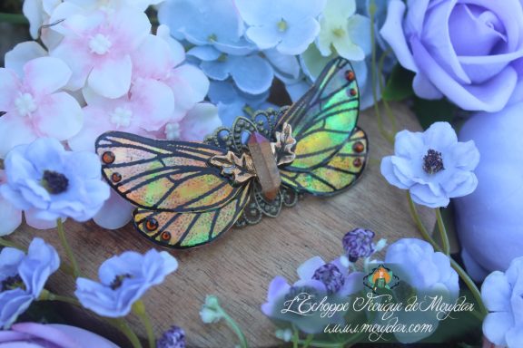 Barrette cheveux ailes de papillon vert et dore, vue rapprochee sur fond de fleurs