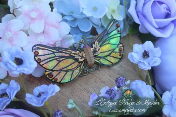 Barrette cheveux ailes de papillon vert et dore, vue rapprochee sur fond de fleurs