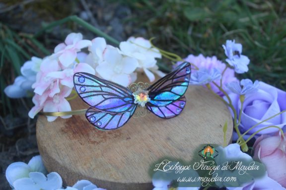 Barrette cheveux petites ailes de papillon bleu violet, posee sur bois avec fleurs