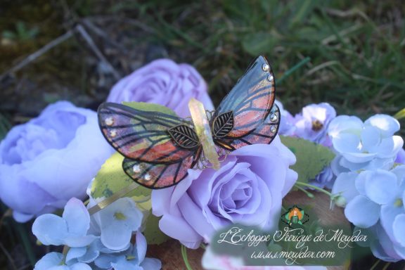 Barrette cheveux ailes de papillon avec strass, posee sur fleurs violettes en exterieur