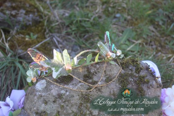 Couronne aile de papillon verte et fleurs, posee sur une pierre moussue