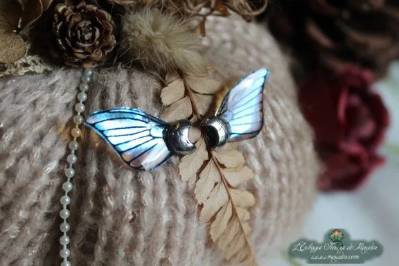 Petite epingle ailes bleues avec perles argentees, sur coussin de laine et fougere