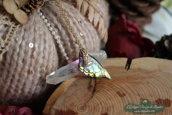 Pendentif aile verte irisee sur chaine doree, presente sur socle en bois avec cristal