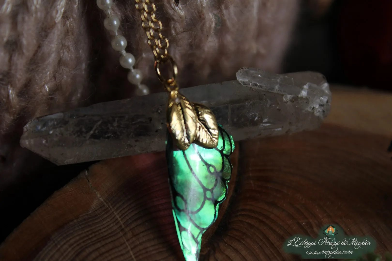 Pendentif aile unique verte, vue rapprochee sur socle en bois avec cristal