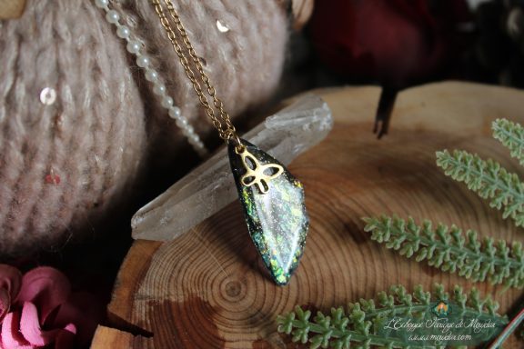 Pendentif aile unique argentee et blanche avec breloque trefle, presente sur socle en bois