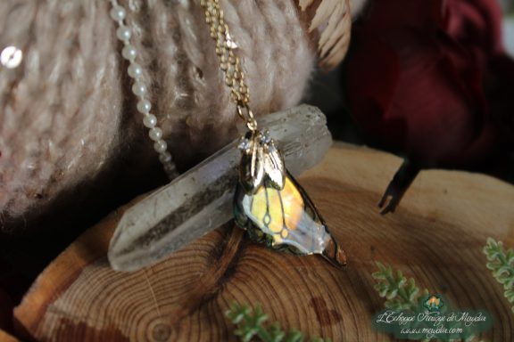 Pendentif aile unique dore et blanche avec breloque feuille, presente sur socle en bois