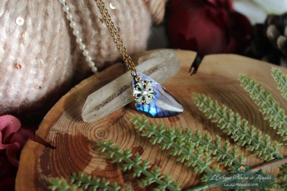 Pendentif aile unique bleue et violette avec breloque flocon, presente sur socle en bois