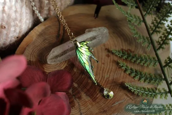 Pendentif fine aile doree avec perle ambree pendante, presente sur socle en bois