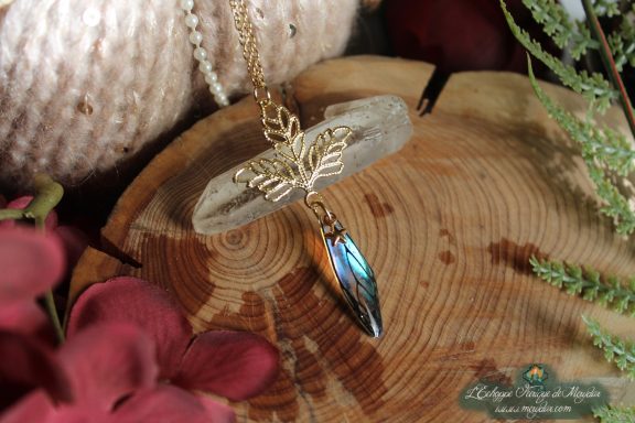Pendentif breloque feuille doree avec aile bleue violette pendante, presente sur socle en bois