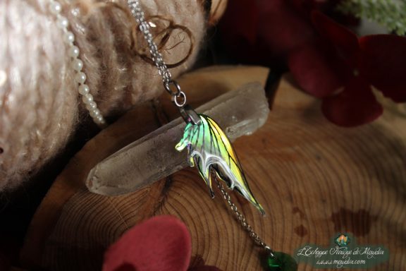Pendentif aile de dragon noire et verte irisee, presente sur socle en bois