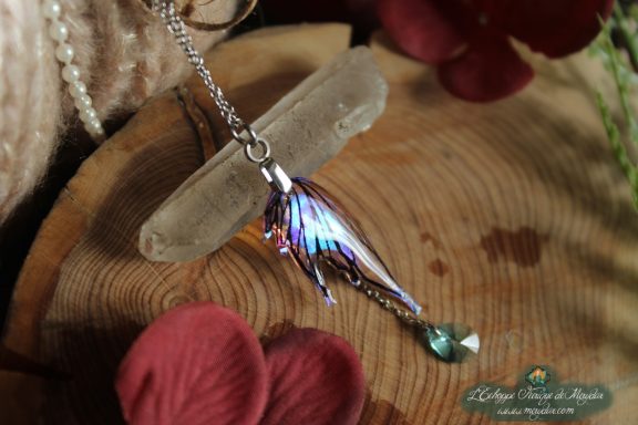 Pendentif aile de dragon violette bleue avec perle pendante, presente sur socle en bois