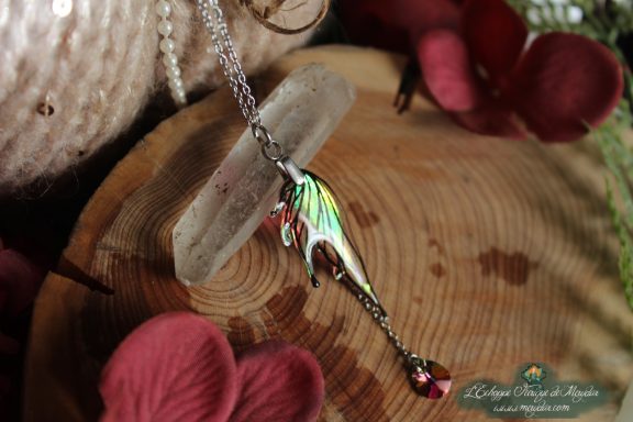 Pendentif aile de dragon verte doree avec perle rouge pendante, presente sur socle en bois