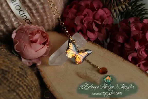 Collier pendentif papillon orange et noir entier avec perle ambree, presente sur socle en bois fleuri