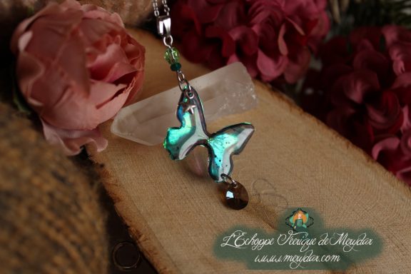 Collier pendentif papillon turquoise entier avec perle brune, presente sur socle en bois fleuri