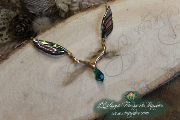 Collier pendentif branche doree avec deux ailes vertes et perle turquoise, gros plan sur bois