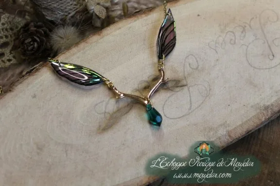 Collier pendentif branche doree avec deux ailes vertes et perle turquoise, gros plan sur bois