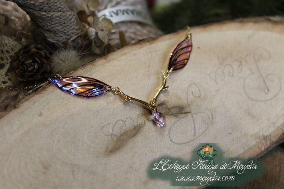 Collier pendentif branche doree avec deux ailes bleues violettes, gros plan sur bois