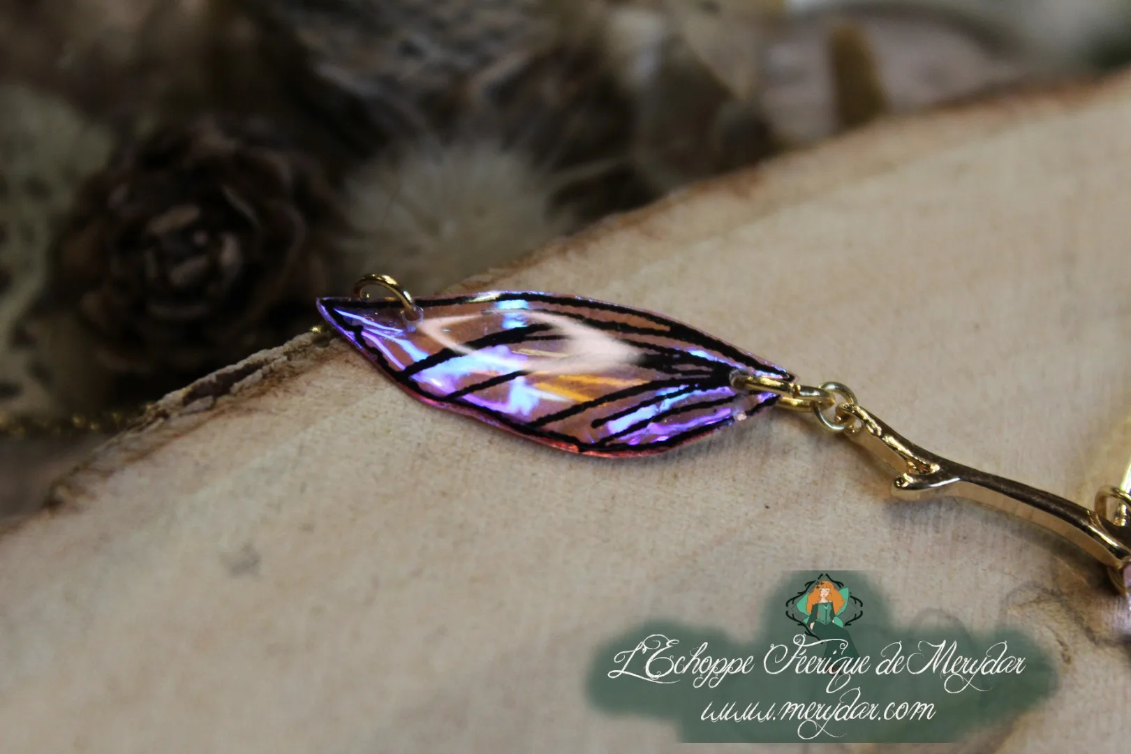 Collier pendentif branche doree avec deux ailes violettes et dorees, gros plan sur bois