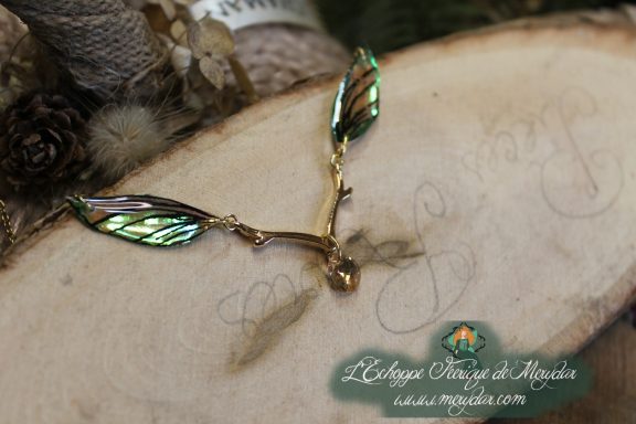 Collier pendentif branche doree avec deux ailes vertes, gros plan sur bois