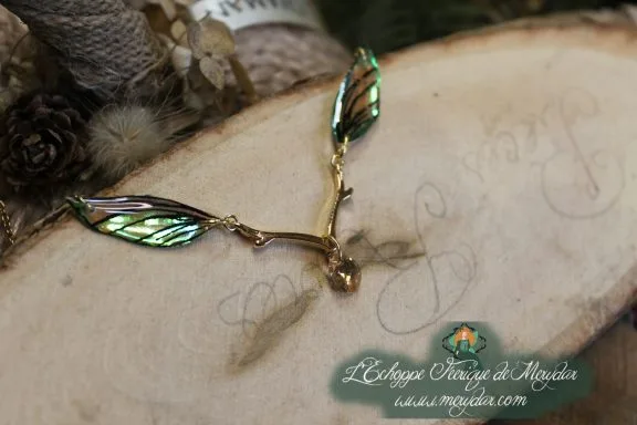 Collier pendentif branche doree avec deux ailes vertes, gros plan sur bois