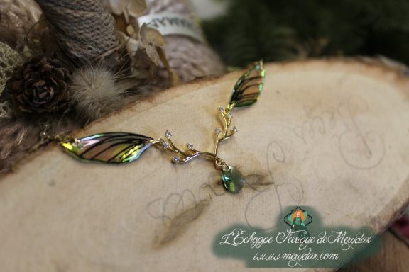 Collier pendentif branche doree avec deux ailes turquoise vertes et perle turquoise, gros plan sur bois