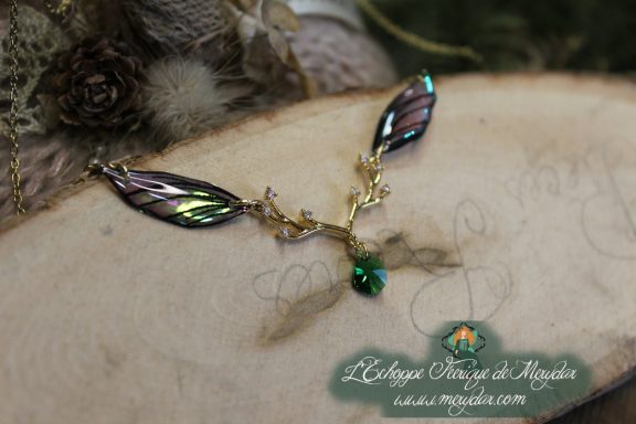 Collier pendentif branche doree avec deux ailes noires vertes et perle verte, gros plan sur bois