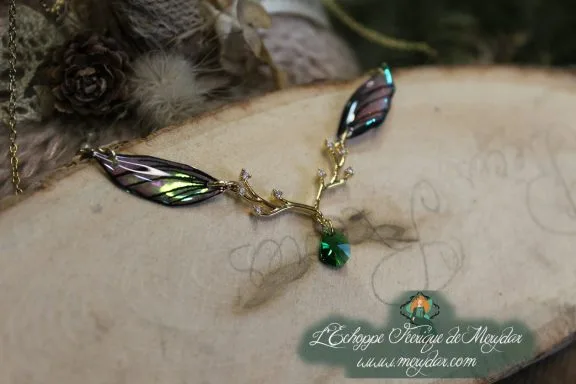 Collier pendentif branche doree avec deux ailes noires vertes et perle verte, gros plan sur bois