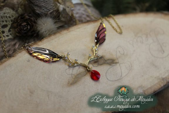 Collier pendentif branche doree avec deux ailes noires brunes et perle rouge, gros plan sur bois