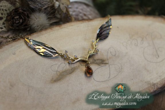 Collier pendentif branche doree avec deux ailes brunes dorees et perle ambree, gros plan sur bois