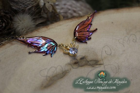 Collier pendentif deux ailes brunes et violettes avec breloque cristal, gros plan sur bois