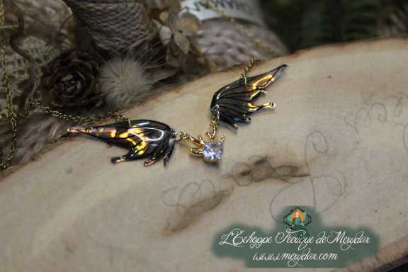 Collier pendentif deux ailes noires et dorees avec breloque cristal, gros plan sur bois