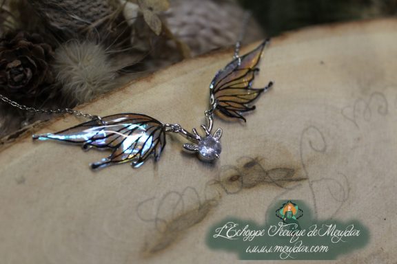 Collier pendentif deux ailes dorees et bleues avec breloque cristal, gros plan sur bois