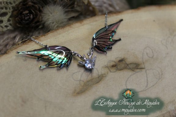 Collier pendentif deux ailes brunes et blanches avec breloque cristal, gros plan sur bois