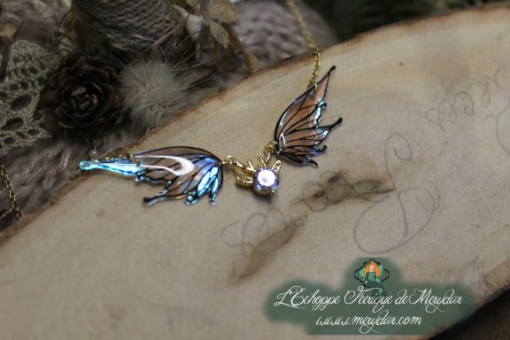 Collier pendentif deux ailes bleues et blanches avec breloque cristal, gros plan sur bois