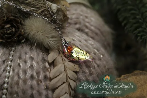 Pendentif aile texture ecailles ambree sur chaine argentee, gros plan sur fougere