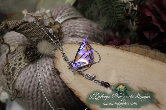 Pendentif papillon violet avec chainettes pendantes, gros plan sur bois
