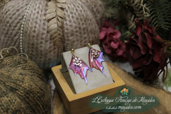 Boucles d'oreilles ailes depareillees roses et bleues, presentees sur socle en bois