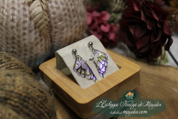 Boucles d'oreilles ailes de papillon violettes, presentees sur socle en bois