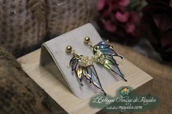 Boucles d'oreilles ailes de fee dorees, presentees sur socle en bois