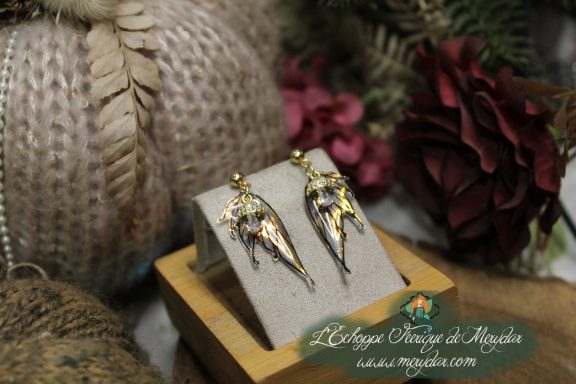 Boucles d'oreilles ailes de fee dorees, presentees sur socle en bois variante