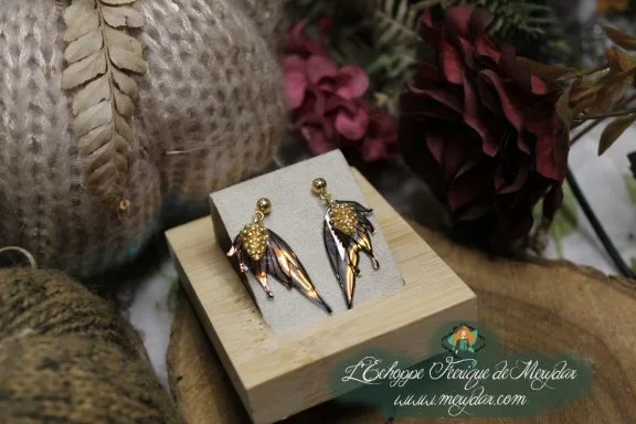 Petites boucles d'oreilles ailes de fee dorees, presentees sur socle en bois
