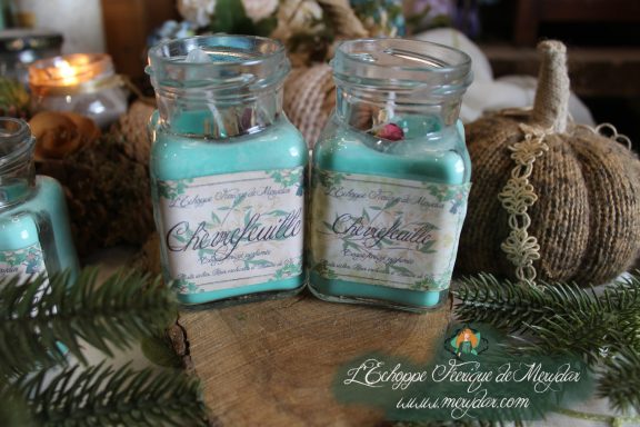 Flacons Chevrefeuille et bougies en pot presentes ensemble sur bois avec bougie allumee