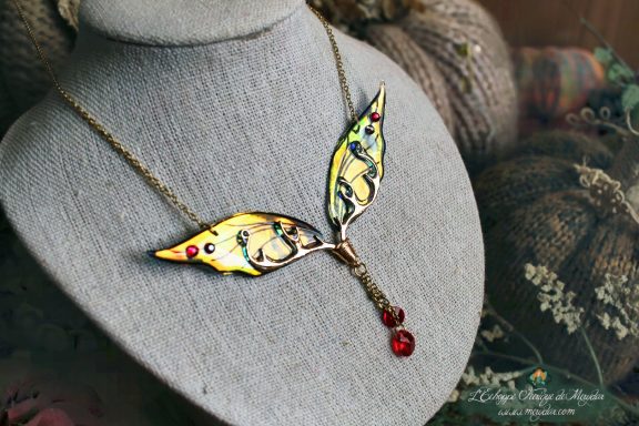 Collier pendentif branche doree avec aile jaune et perle rouge, presente sur buste