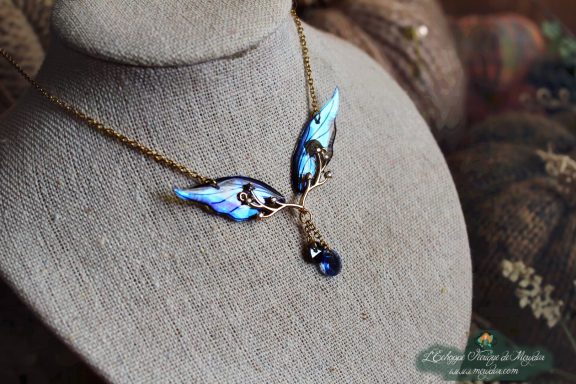 Collier pendentif branche doree avec aile bleue et perle bleue, presente sur buste porte-bijoux