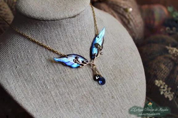 Collier pendentif branche doree avec aile bleue et perle bleue, presente sur buste porte-bijoux