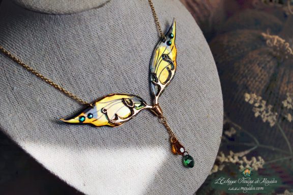 Collier pendentif branche doree avec deux ailes jaunes et perle verte, presente sur buste